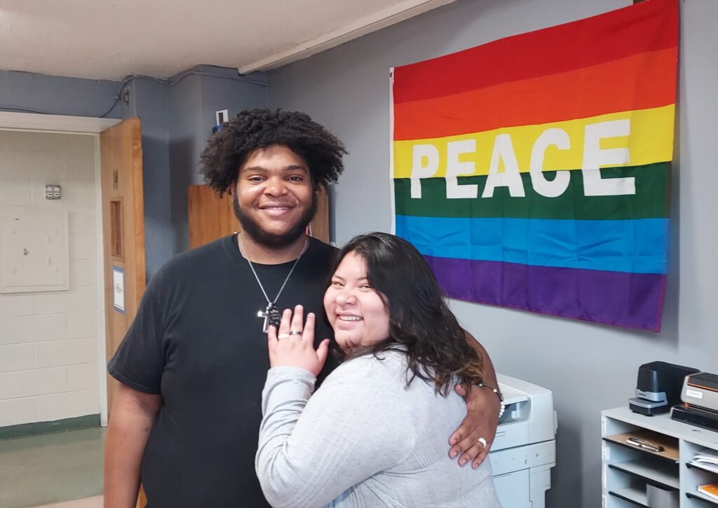 Jason Kea, posing with an Asian woman in front of a rainbow flag with the word PEACE